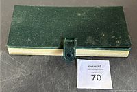 Closed green leatherette hinged case with a clasp showing wear and light spotting on the surface.