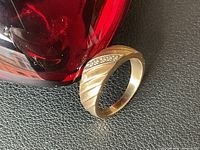10k gold ring leaning against a red vase showing the diagonal striped pattern and diamond spray across the band