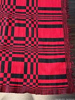 Corner view showing red and black geometric pattern with knotted fringe
