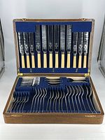 Complete view of antique stainless nickel silver cutlery set laid in open oak box with blue velvet holder showing dinner knives in lid and forks, spoons and teaspoons in base.