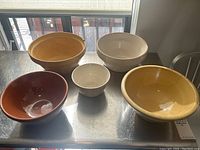 Lot of 5 antique mixing bowls including yellow ware and Medalta. Bowls show signs of use, including crazing and wear.