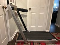 Side view of treadmill upright showing silver frame, black belt, foam-padded handlebars
