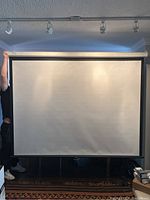 Full frontal view of screen fully extended showing white vinyl projection surface and casing