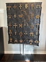 Front view of the full sculpture showing black textured canvas with wooden inlay patterns on steel stand