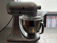 Front left view of silver KitchenAid Artisan stand mixer with bowl and pouring shield