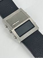 Angled front view showing stainless steel case with mesh speaker grille and LCD display