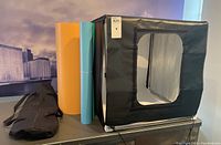 Items included with the lightbox: three colored dropsheets (orange, light blue, white) and a black carry bag