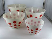 Four vintage FireKing red polka dot mixing bowls grouped together showing size sizes and pattern.
