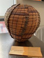 Full side view of spherical coiled basket on tabletop with paper envelope showing maker’s name