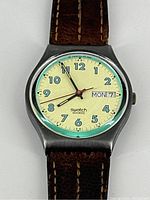 Front close-up of vintage Swatch wristwatch showing cream dial with black numerals, day and date window, and leather strap.