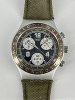 Front close-up of vintage Swatch Irony Aluminium chronograph watch face showing black dial with three subdials and engraved metallic bezel, canvas strap partially visible.