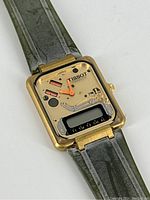 Close-up of gold-tone square skeleton dial with orange hands, digital display at bottom, TISSOT logo at 12 o’clock