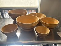 Set of six vintage yellow ware mixing bowls arranged in two rows, showing the variety in size and shape with embossed swirl patterns and brown accents.