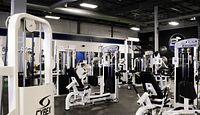 Gym interior showing white Cybex and Atlantis strength machines against black rubber flooring