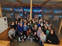 Group photo of guests standing in front of multiple axe throwing lanes with targets and electronic scoring displays