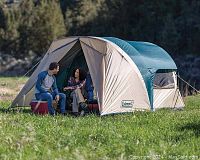 Outdoor photo of the Coleman 6-person cabin tent setup showing spacious entry and two people sitting in front.