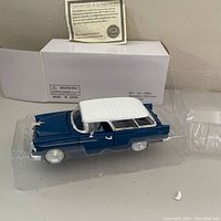 Photo of diecast 1955 Chevy Bel Air Nomad model car in blue with white roof, inside clear plastic protective casing and sitting atop white box with item info on side. Certificate of Authenticity placed behind the model car.