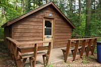 Cedar cabin exterior in forest with front deck and wooden bench seating