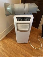 Photo showing white rectangular portable air conditioner with exhaust hose and window vent adapter attached on top.