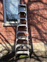 Aluminum step ladder standing upright against a brick wall, showing front view with 7 steps and a top platform.