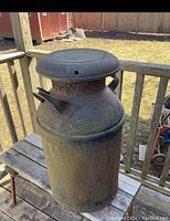 Front side view of the antique metal milk can showing lid, handles, and weathered surface with rust and patina.