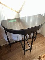 Full view of the half moon shaped wooden side table showing the shape and finish of the top and the turned legs.