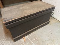 Side angle view of the antique wooden trunk showing lid, hinges, and base details.