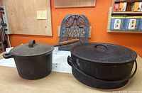 Photo showing small and large cast iron pots with lids and cast iron grate in the background on a table.