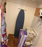 Ironing board, furnace filters, organizing cart with cleaning supplies and aprons visible hanging on left side.