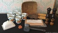 Full view of lot items including mugs, butter dish, cedar planks, bacon press, shakers, mallet, bear, bowl, napkin holder.
