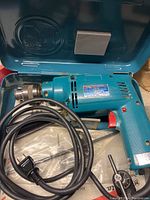 Blue Makita electric hammer drill with power cord inside blue plastic case with Makita logo.