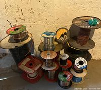 Multiple spools of assorted electrical wire stacked on the floor showing copper, black, and colored wires on wooden and plastic spools.