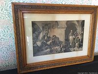 Overall view of the framed artwork on floral wallpaper background, showing carved wooden frame and framed image inside.