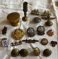Overview of 22 military-themed buttons, pins, insignia and decorative brass items on fabric background.