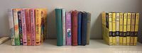 Wide shot showing a series of hardcover books including Nancy Drew, Trixie Belden, and Charlie Brown titles along with yellow metal bookends on a white surface.