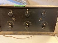 Front view of the wooden transmitter showing six control knobs and the printed gauges for tuning.