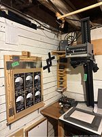 Wide view showing the Omega Super Chromega C picture enlarger mounted on a vertical stand along with a control panel and various photography accessories on a wooden wall shelf.