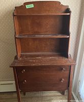Front view of wooden dresser with two upper shelves, drop door closed and two drawers below, showing scratches on surface.