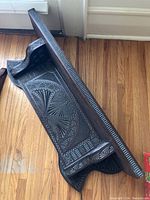 Carved wooden decorative shelf with intricate detailed pattern, lying on hardwood floor.