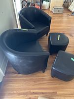 Two black vinyl tub chairs each with its own matching black vinyl footstool, all placed on wood floor.