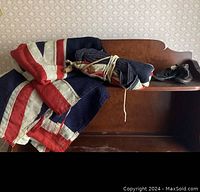 Three folded vintage cloth flags, one tied with string, placed on a wooden bench with infant shoes to the side.