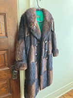 Full view of brown multi-tone fur coat hanging, showing knee-length and double-breasted style.