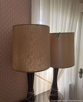 Photo showing both vintage table lamps side by side with beige cylindrical textured lamp shades and narrow black ceramic bases with white vertical crackle lines.