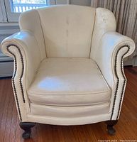 Front view of white club chair showing upholstery studs and wooden legs.