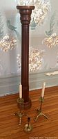 Wooden candle stand with two brass holders and one single brass holder arranged on wooden floor in front of floral wallpaper