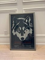 Full view of the framed wolves exhibition poster leaning against a white wall showing the wolf graphic and bilingual text.