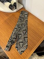 Full view of the gray silk tie with a heart and cherub patterned design rolled out on a wooden table.
