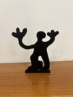Single figurative tea light holder showing stylized human figure shape with raised hands and integrated candle cup on wooden surface with white background.