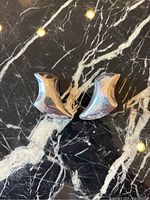 Pair of curved sterling silver clip-in earrings photographed on black marble surface to show reflective shine and sculptural form.