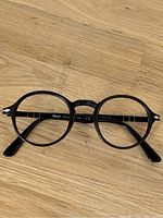 Front-facing view of dark tortoiseshell round frame Persol Typewriter Edition glasses on wooden surface.